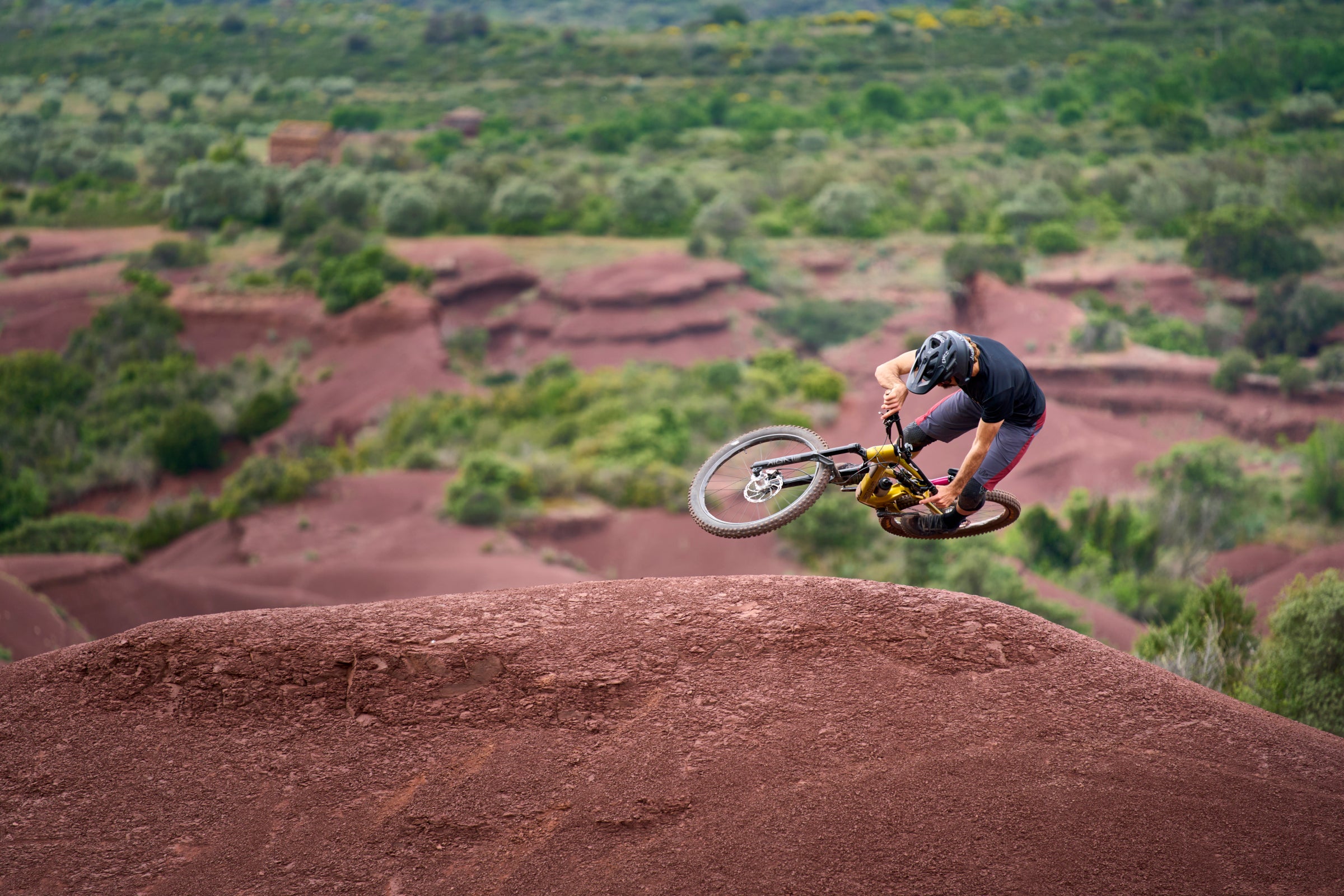 Mountain biker pulling a whip over a red dirt jump